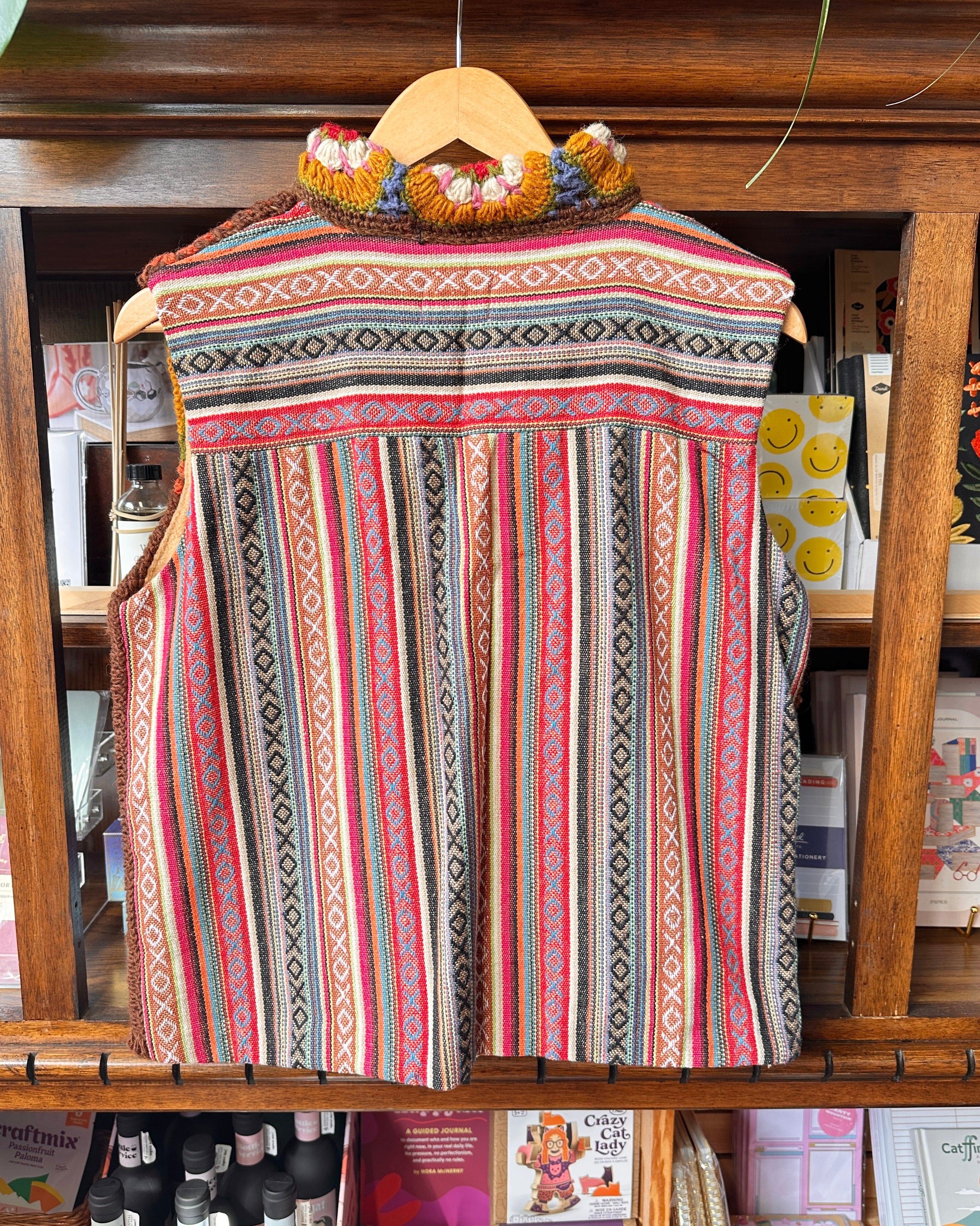 A sleeveless bohemian-style woven vest with vertical stripes and geometric patterns in pink, red, green, black, and beige.