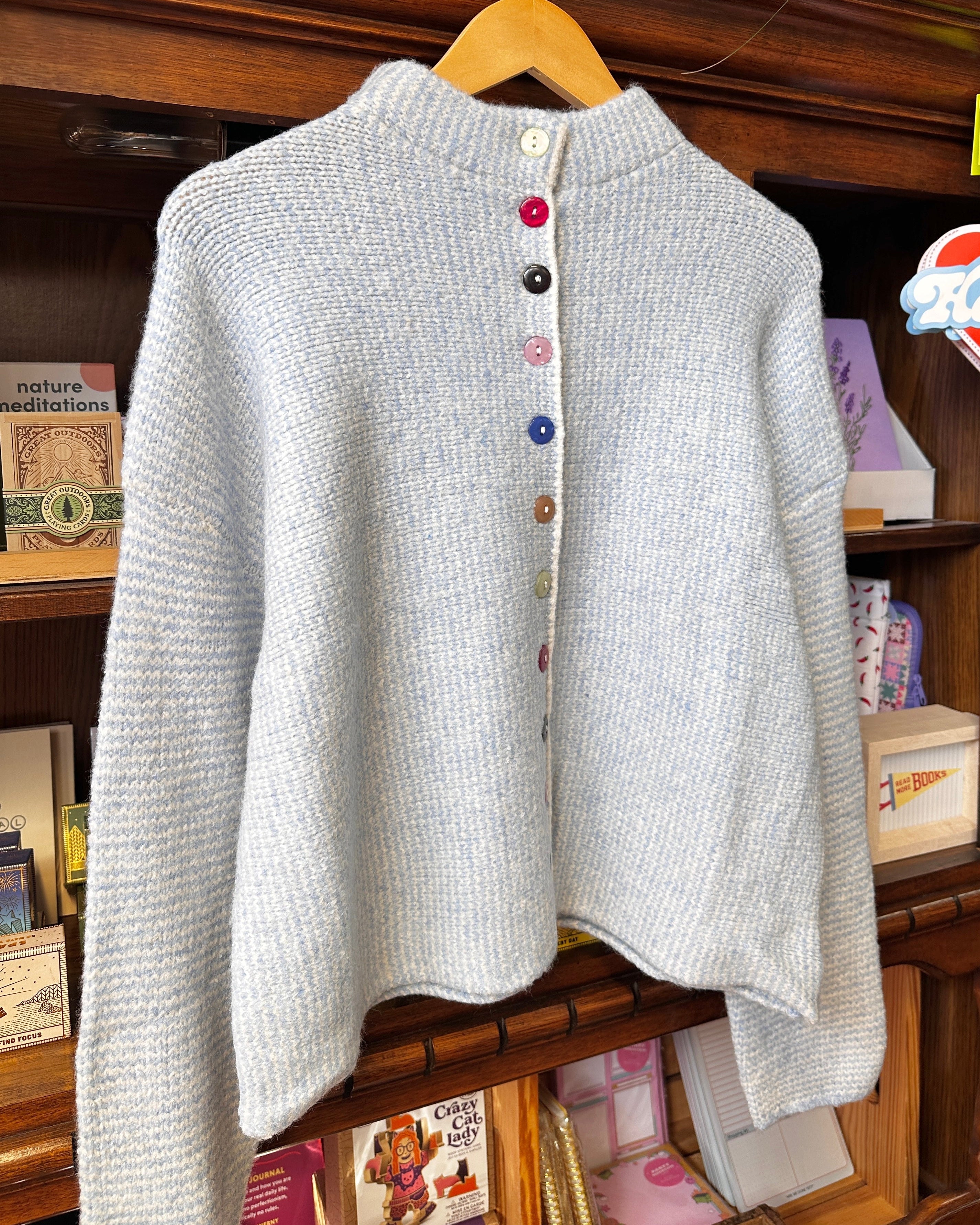 A light blue and white striped textured knit cardigan sweater with a high mock neck and colorful decorative buttons.