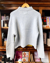 The back of a light blue and white striped textured knit cardigan sweater with a high mock neck.