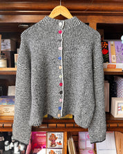 A black and white textured knit cardigan sweater with colorful decorative buttons.