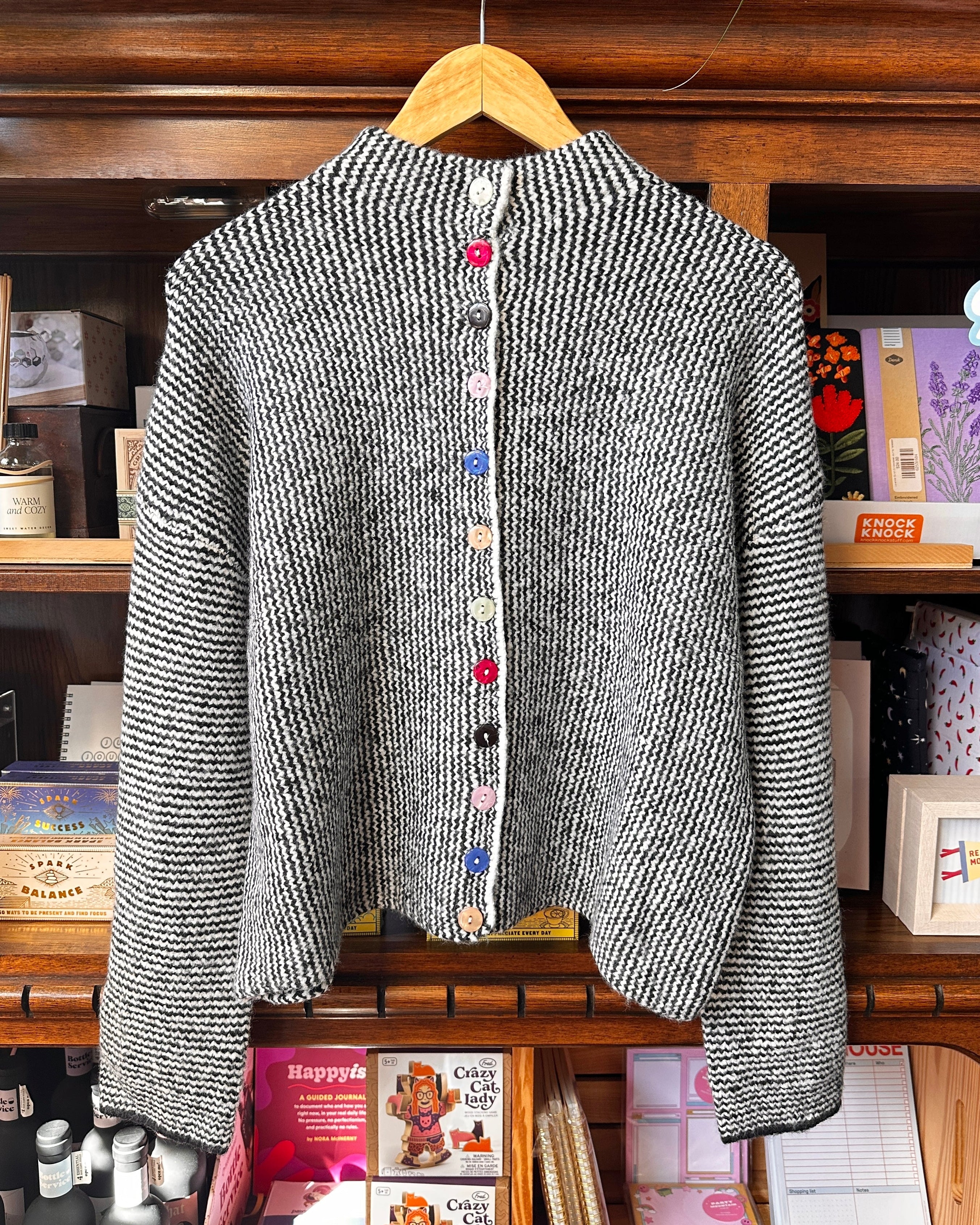 A black and white textured knit cardigan sweater with colorful decorative buttons.