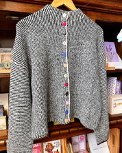 A black and white textured knit cardigan sweater with colorful decorative buttons.