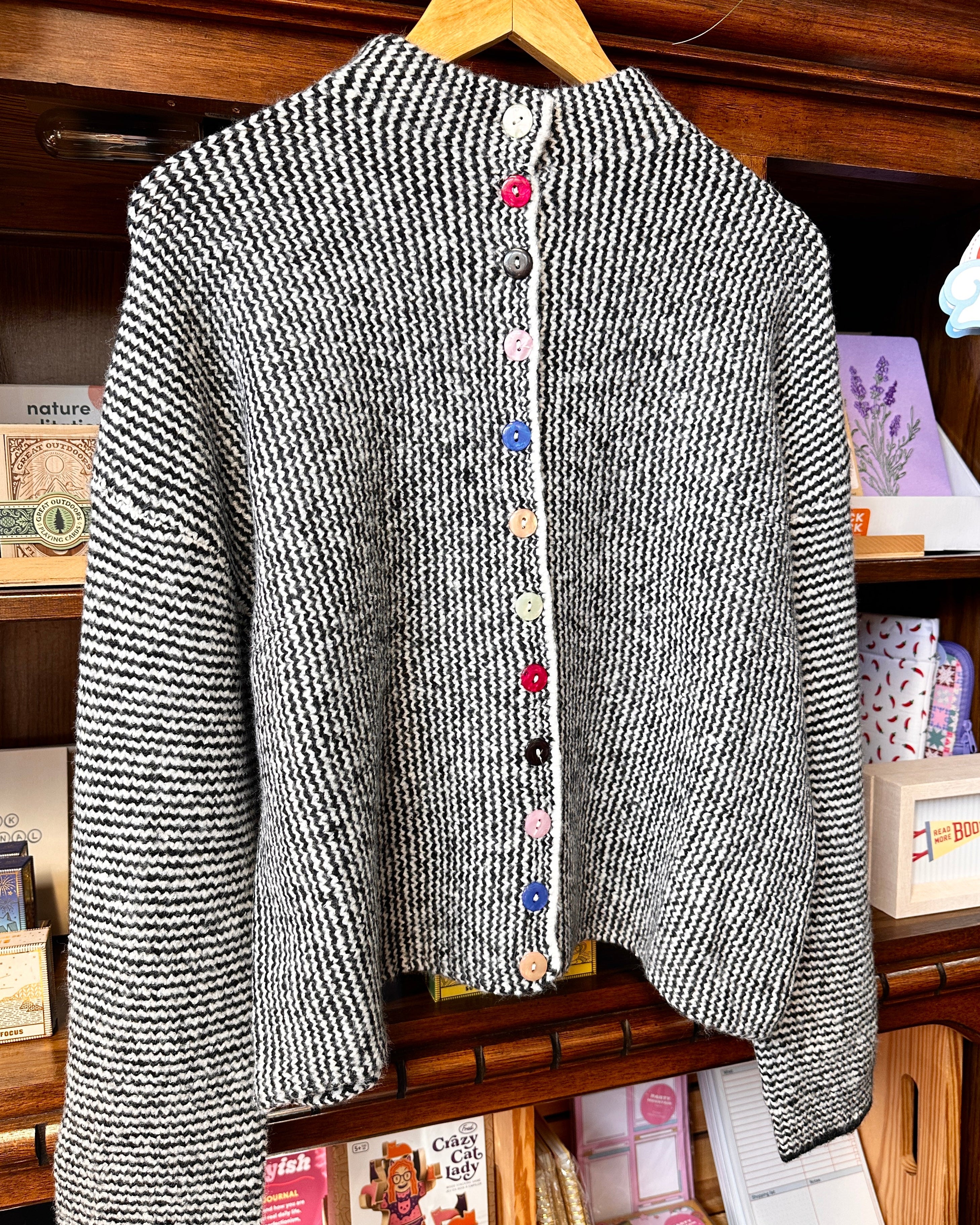 A black and white textured knit cardigan sweater with colorful decorative buttons.