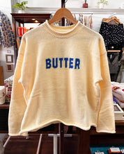 A yellow-colored fuzzy knit sweater with the word 'BUTTER' in blue letters across the chest.