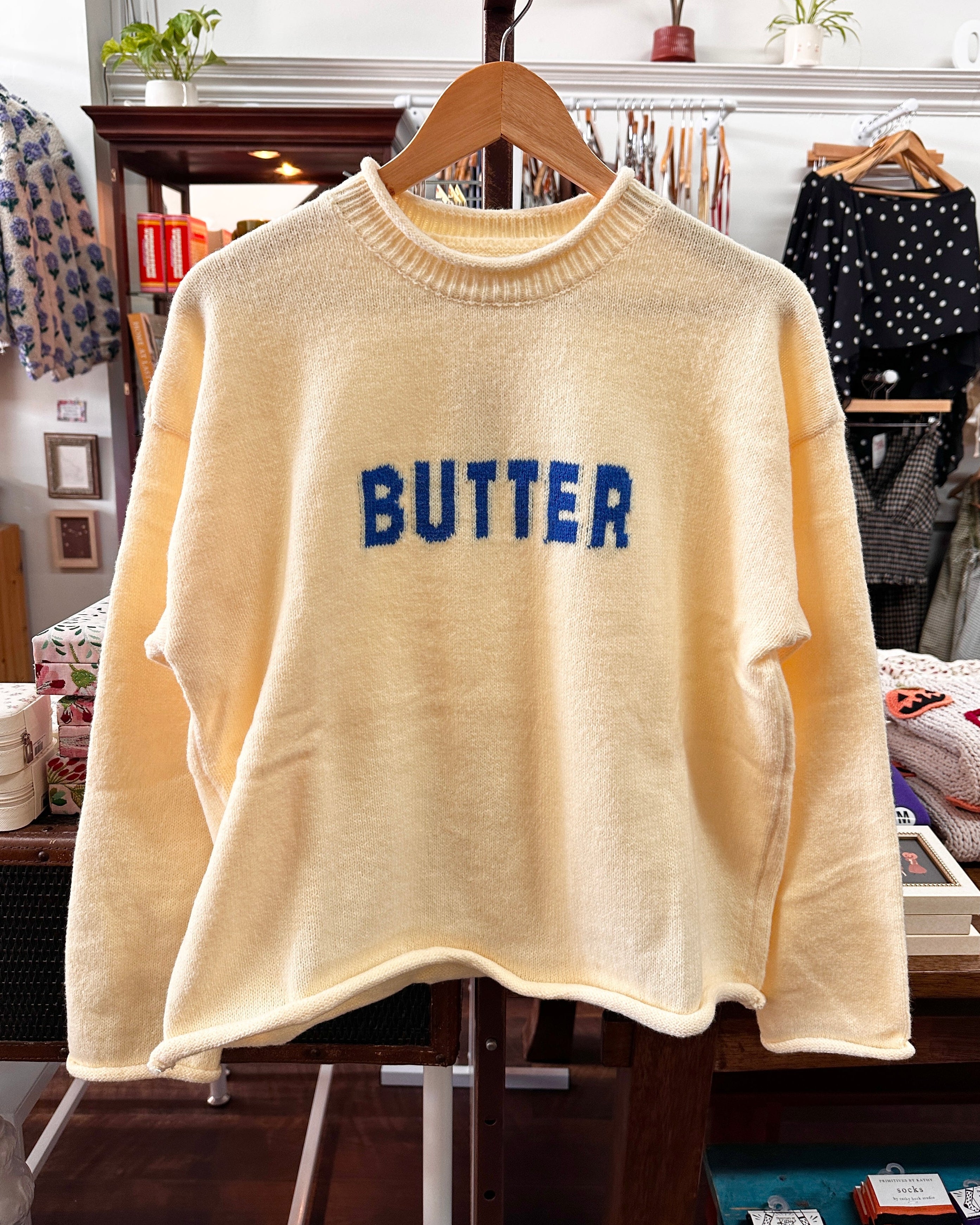 A yellow-colored fuzzy knit sweater with the word 'BUTTER' in blue letters across the chest.