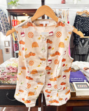A sleeveless cream-colored vest with a colorful autumn-themed print of pumpkins, acorns, and treats.