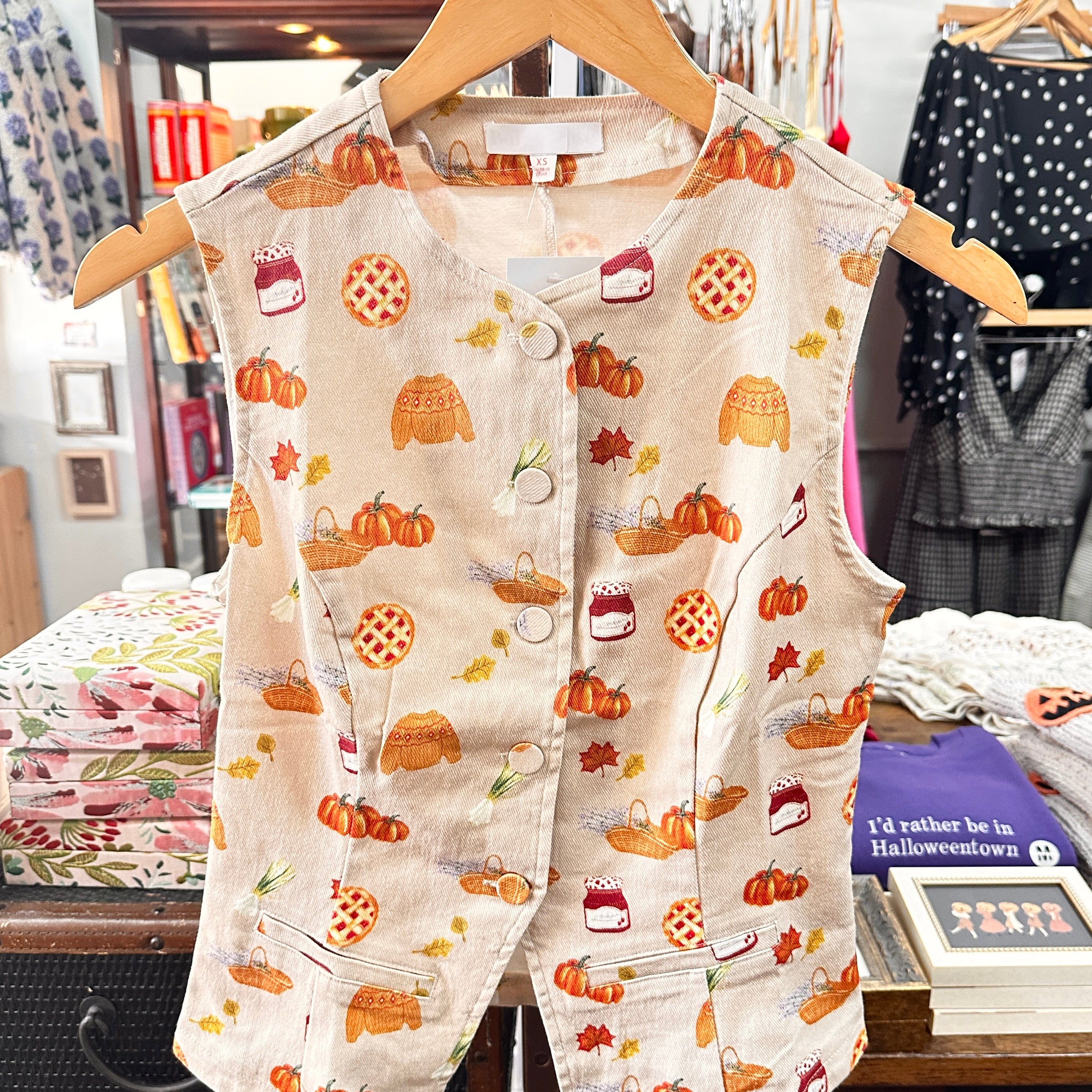 A sleeveless cream-colored vest with a colorful autumn-themed print of pumpkins, acorns, and treats.