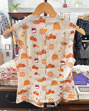 A sleeveless cream-colored vest with an autumn pumpkin and acorn print.