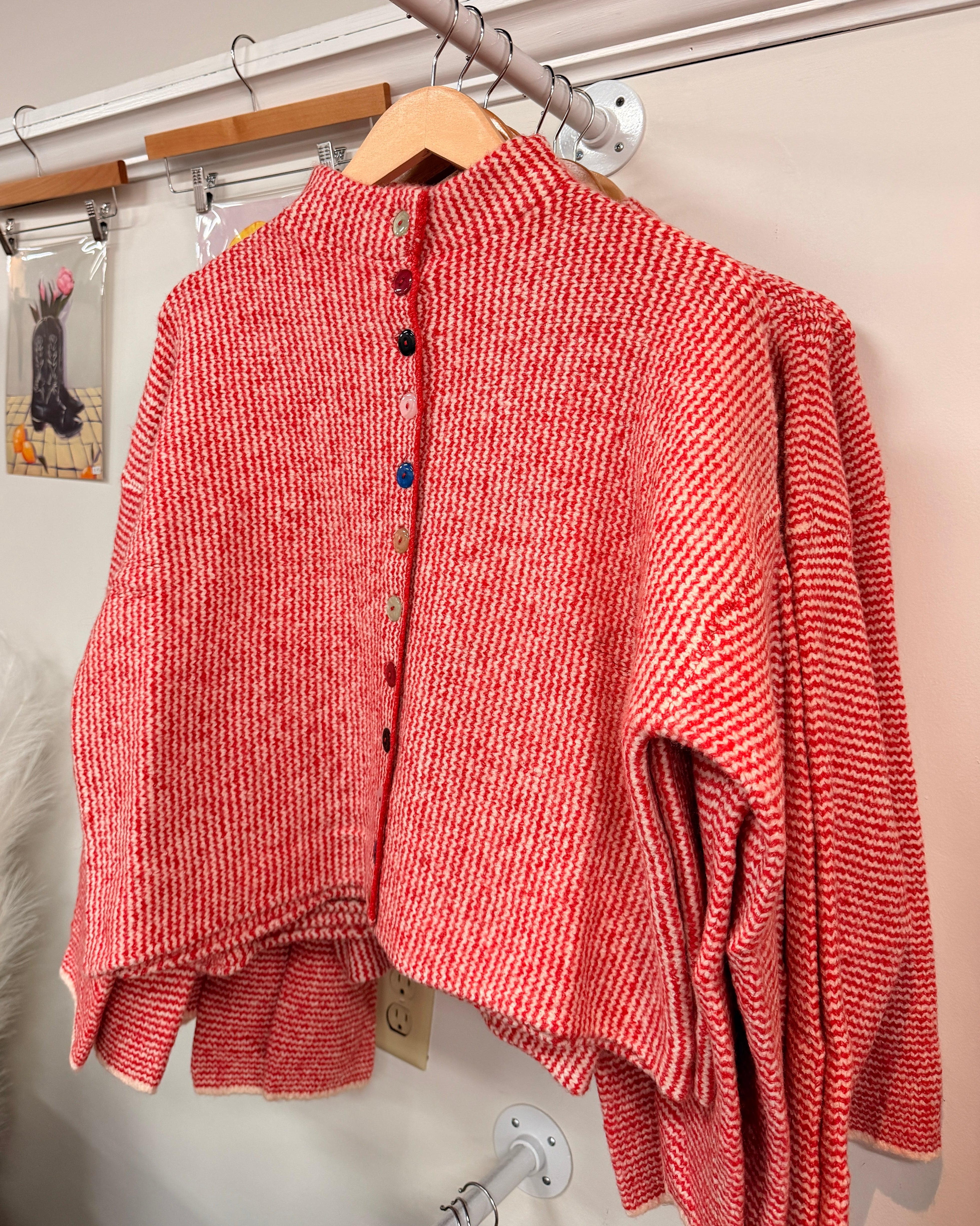 A red and white striped knit cardigan with a high mock neck and colorful decorative buttons down the front.