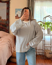 A woman takes a mirror selfie in a bedroom, wearing a striped long-sleeve shirt and light blue wide-leg jeans.