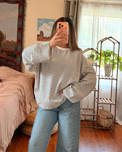 A woman takes a mirror selfie in a bedroom, wearing a striped long-sleeve shirt and light blue wide-leg jeans.