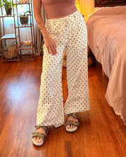 A woman wearing cream wide-leg pants with small black polka dots.