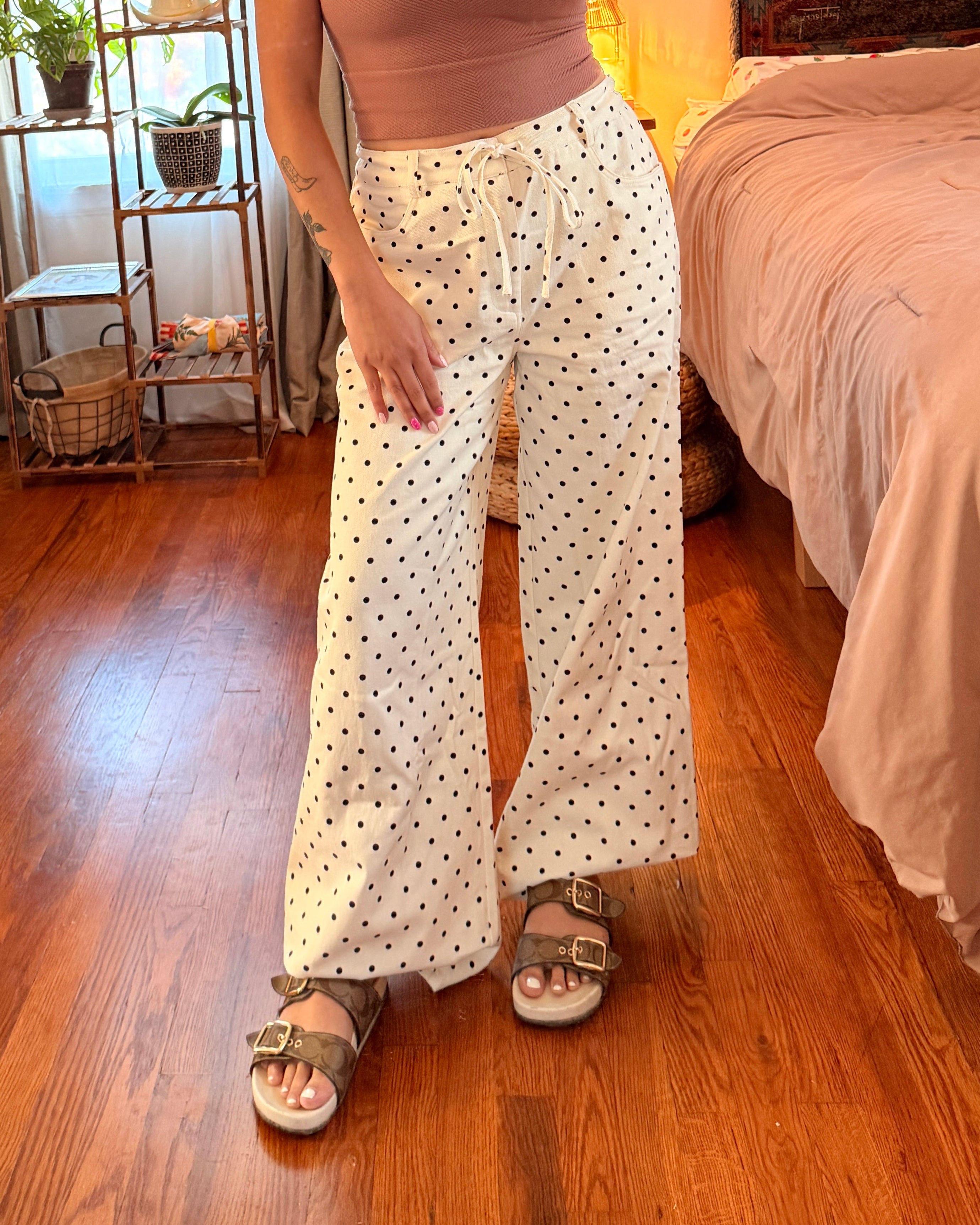 A woman wearing cream wide-leg pants with small black polka dots.